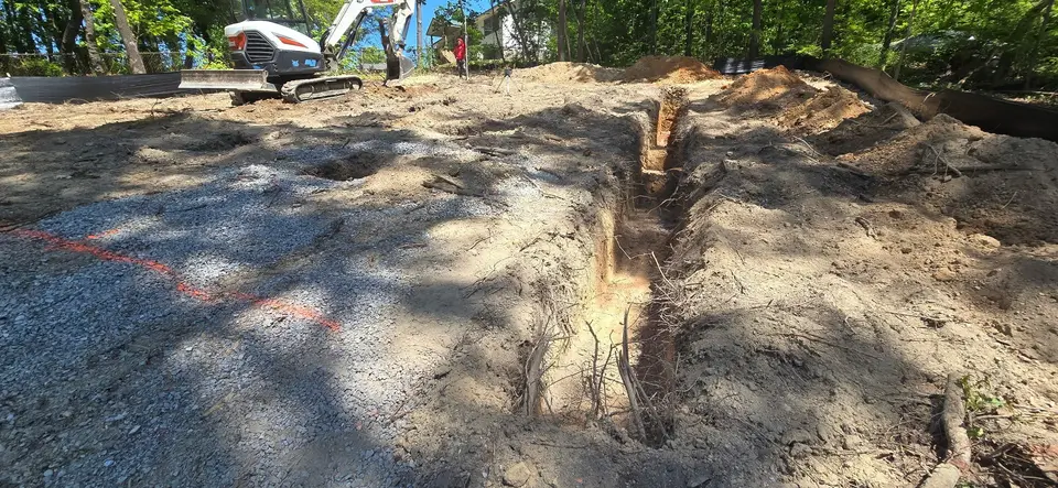 Open trench cut across a graded lot, excavator in the background