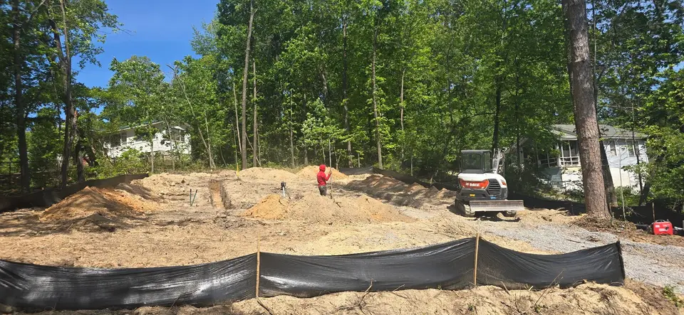New-construction lot graded for the building pad, with silt fence and an excavator on site