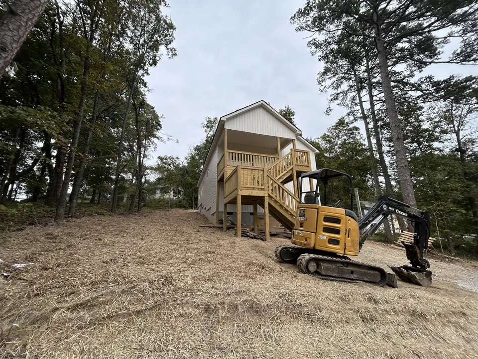 Mini excavator grading a hillside lot in front of a new two-story home