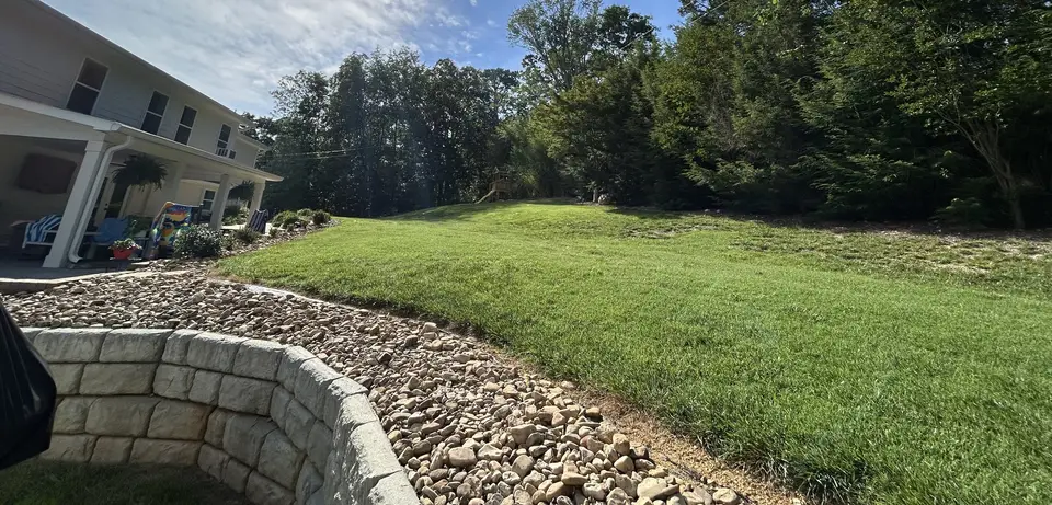 Rock-lined drainage swale beside a block retaining wall