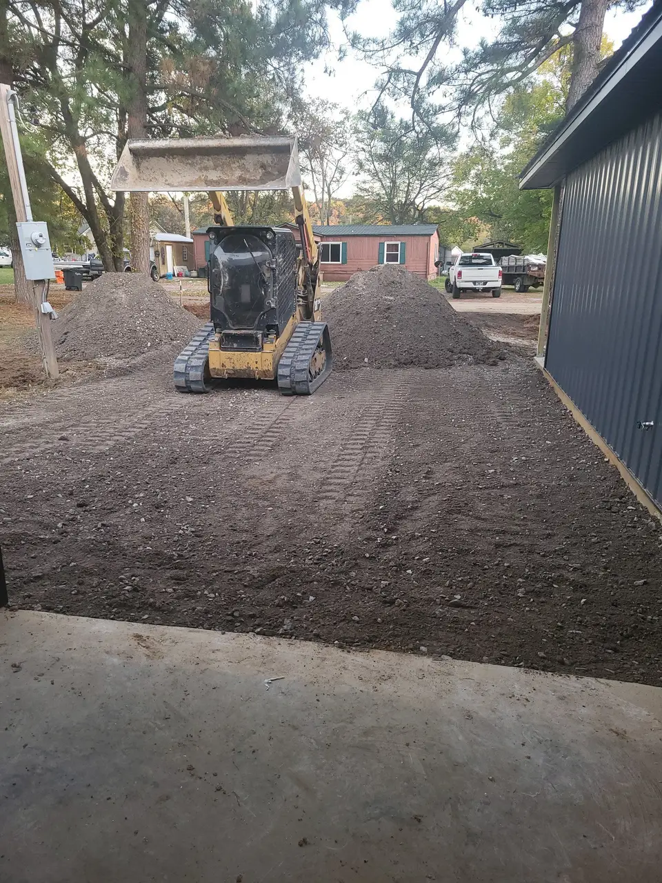 Skid steer spreading dirt beside a building